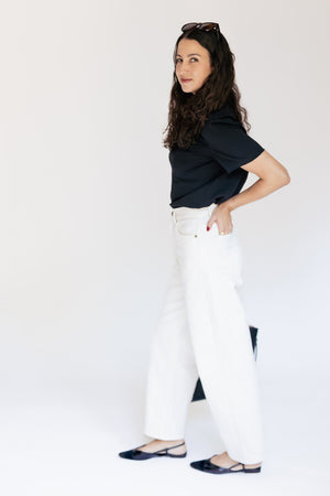 A woman modeling a black short-sleeve top and white wide-leg pants against a plain white studio background.