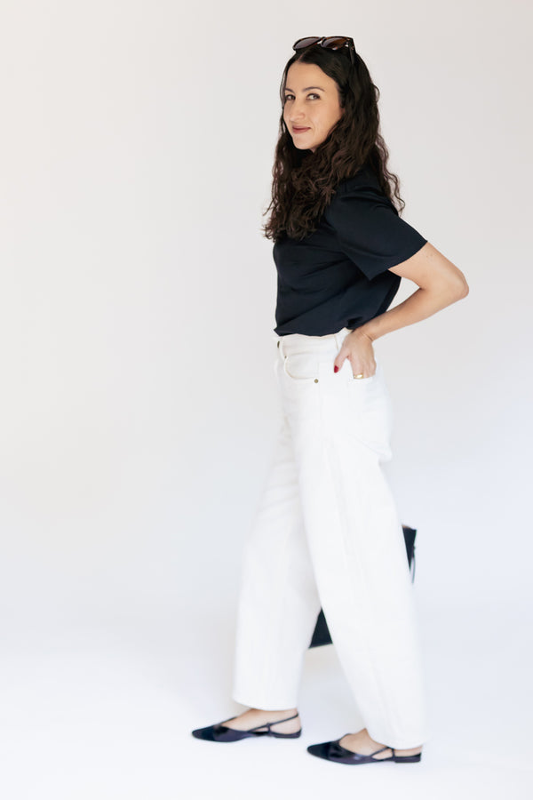A woman modeling a black short-sleeve top and white wide-leg pants against a plain white studio background.