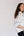 A woman with long dark hair is shown in profile against a plain light background, wearing a loose white shirt with thin dark piping and dark pants.