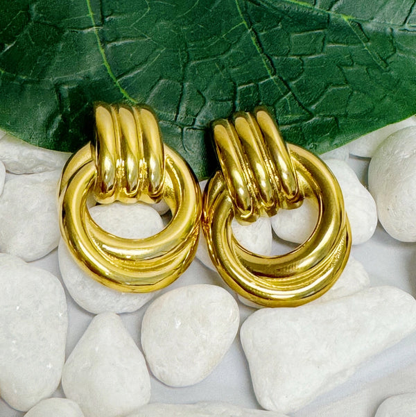 Gold hoop earrings on white stones with a green leaf background
