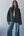 Woman wearing a dark quilted jacket and blue jeans against a plain background