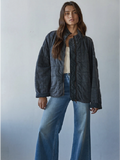 Woman wearing a dark quilted jacket and blue jeans against a plain background