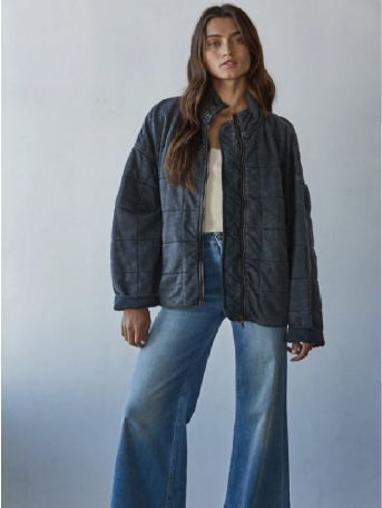 Woman wearing a dark quilted jacket and blue jeans against a plain background