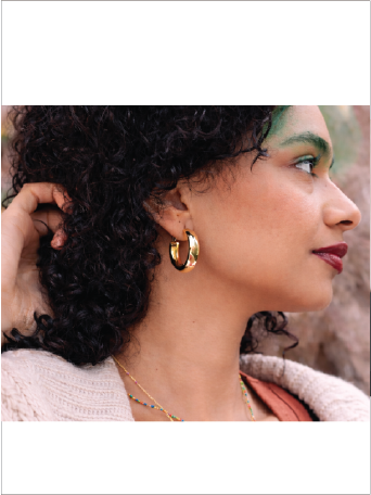 Woman wearing gold hoop earrings with a blurred natural background