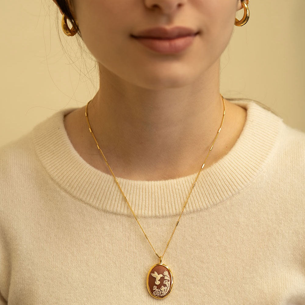 Person wearing a gold necklace with a pendant on a beige background
