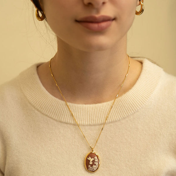 Person wearing a gold necklace with a pendant on a beige background