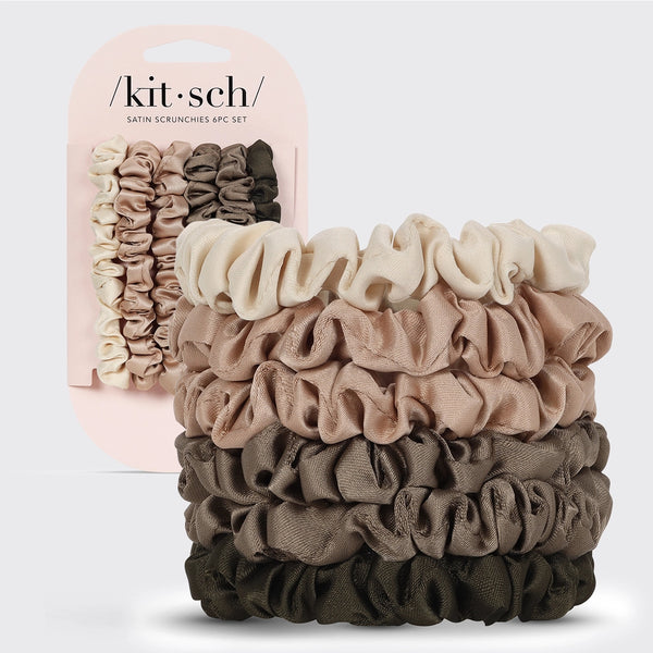 A stack of five satin scrunchies in neutral tones of cream, beige, taupe, brown, and olive green, shown next to their light pink retail packaging card. The brand name 'kit·sch' is visible on the packaging.