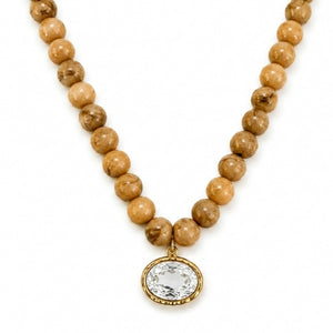 A beaded necklace featuring natural tan and brown stone beads with a gold-toned oval bezel holding a clear faceted gemstone, shown on a plain white background.