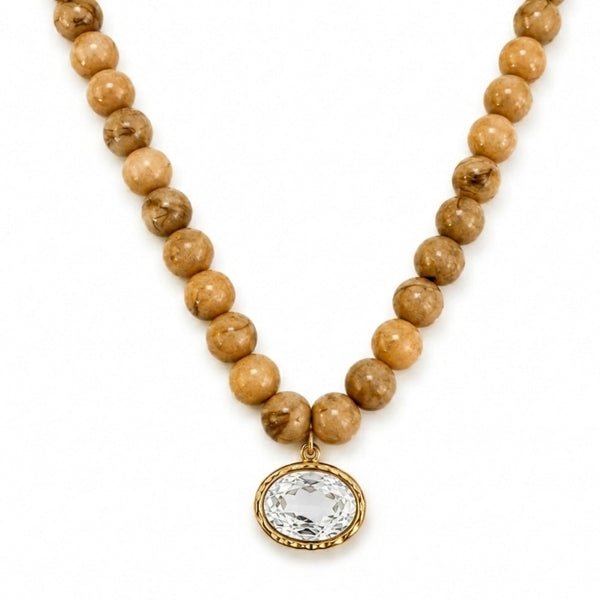 A beaded necklace featuring natural tan and brown stone beads with a gold-toned oval bezel holding a clear faceted gemstone, shown on a plain white background.