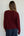 Person wearing a burgundy sweater and dark pants against a white wall