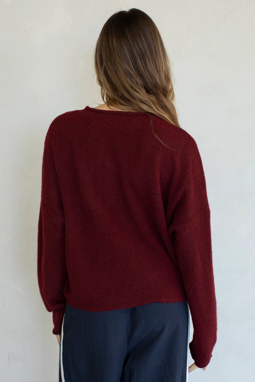 Person wearing a burgundy sweater and dark pants against a white wall