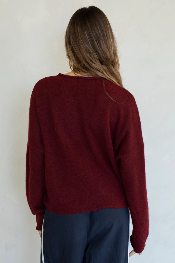 Person wearing a burgundy sweater and dark pants against a white wall