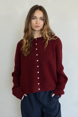 Woman wearing a burgundy sweater with white buttons against a plain background