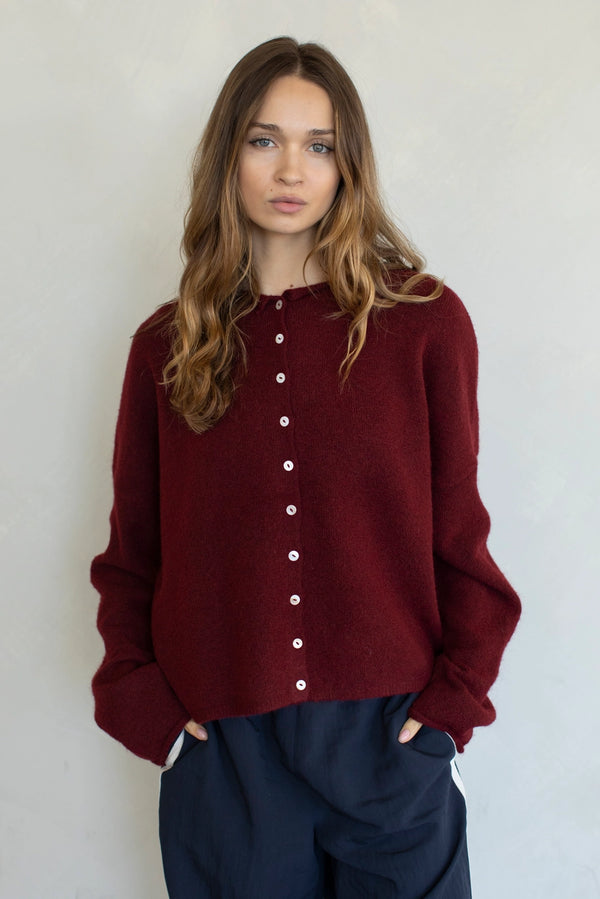 Woman wearing a burgundy sweater with white buttons against a plain background