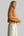 A woman wearing a cropped, long-sleeve knit cardigan in a warm camel brown color with white buttons, paired with light-wash wide-leg jeans.