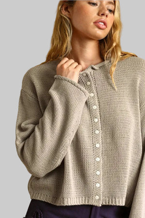 A woman wearing a beige knit button-up cardigan sweater, shown from the chest up against a warm tan background.