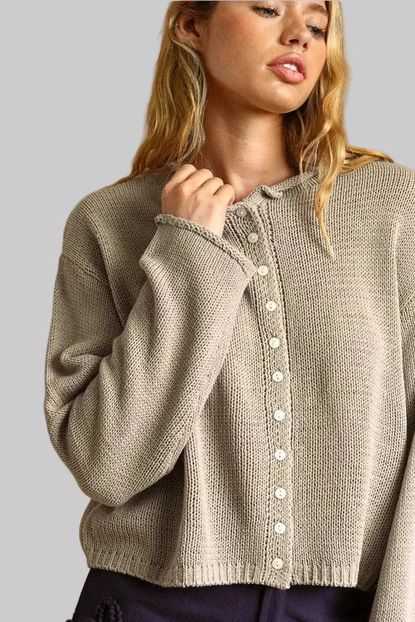 A woman wearing a beige knit button-up cardigan sweater, shown from the chest up against a warm tan background.