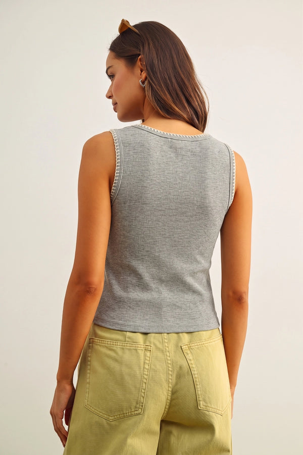 Woman wearing a gray sleeveless top and green pants on a plain background