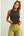 Woman wearing a black sleeveless top and light green pants on a plain background