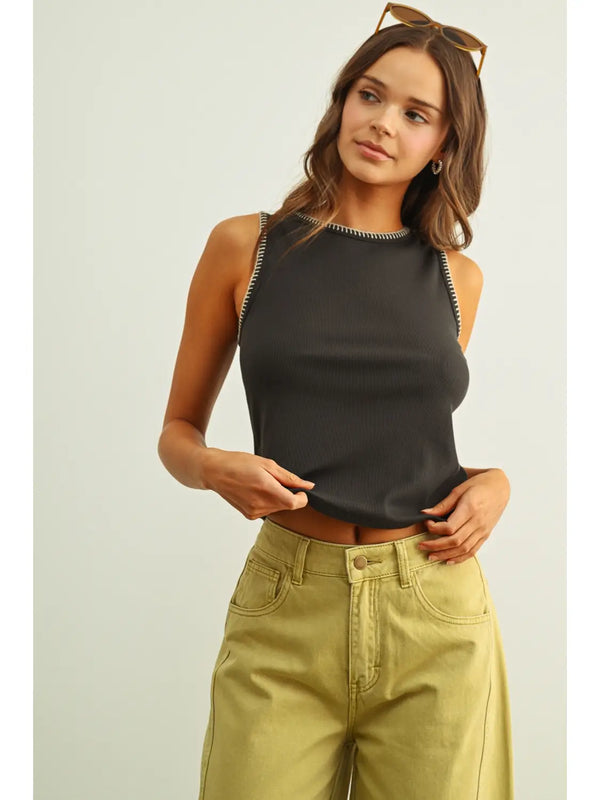 Woman wearing a black sleeveless top and light green pants on a plain background