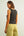 Woman wearing a dark gray tank top with embellishments and light green pants on a plain background