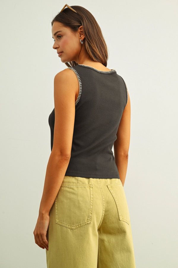 Woman wearing a dark gray tank top with embellishments and light green pants on a plain background