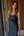 A woman wearing a black satin slip dress, standing in front of a wooden-paneled wall and sliding glass door.