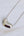 A polished metallic heart-shaped pendant necklace on a delicate silver chain, displayed on a light, textured white surface.