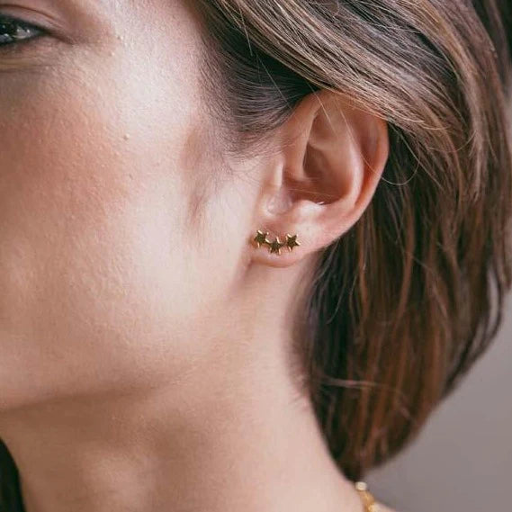 Close-up of an ear wearing a gold earring with small studs.