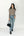 A woman modeling a black and taupe striped mock neck knit top, paired with light blue jeans, black ankle boots, and carrying a black handbag, set against a plain white studio background.
