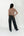 A woman is shown from behind wearing a red and beige horizontally striped long-sleeve turtleneck top, black wide-leg jeans, and black boots, standing against a plain white studio background.