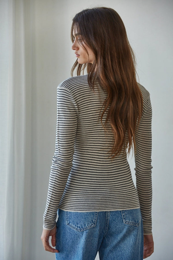 Woman wearing a striped long-sleeve top and blue jeans against a plain background