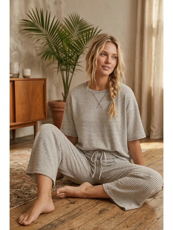 Woman in striped pajamas sitting on a wooden floor with a plant and wooden cabinet in the background.