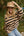 Woman wearing a beige and black striped sweater and tan hat outdoors.