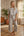 Woman wearing a striped outfit in a home setting with a plant and wooden floor.