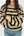 A woman wearing a beige knit sweater with bold black horizontal stripes, paired with blue jeans, shown from the neck down against a plain white background.